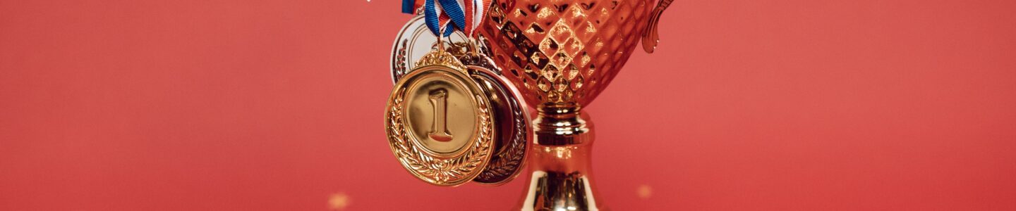 Golden trophy adorned with medals on a red backdrop surrounded by scattered confetti.